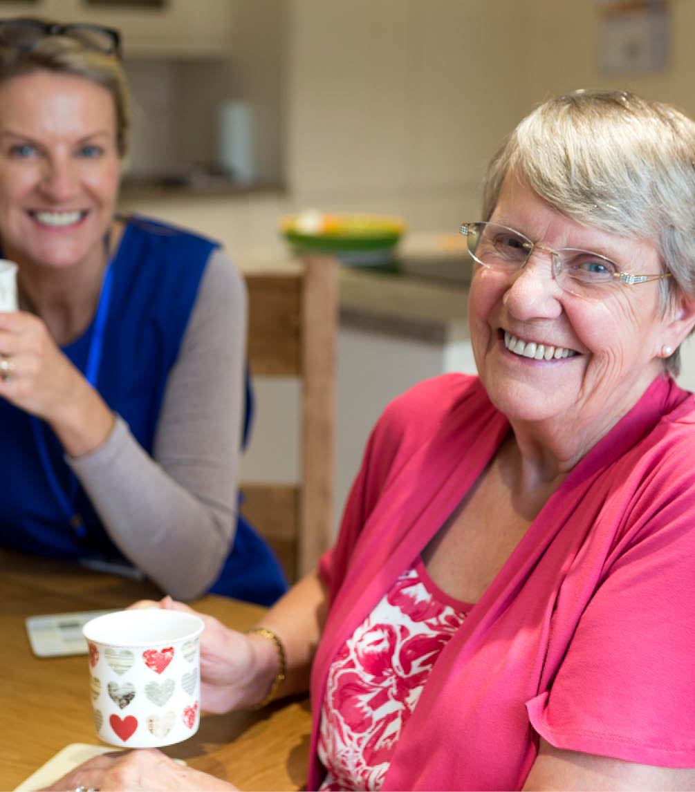 Young woman having a cup of tea with an elderly lady, both smiling