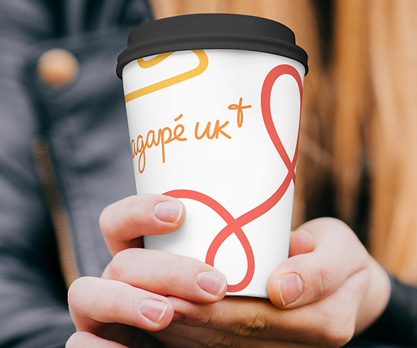 A woman's hands holding a coffee cup, showing the Agape logo and branding