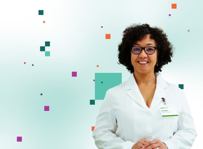 A pharmacist in a white coat in front of a Community Pharmacy England background featuring a pattern of coloured squares