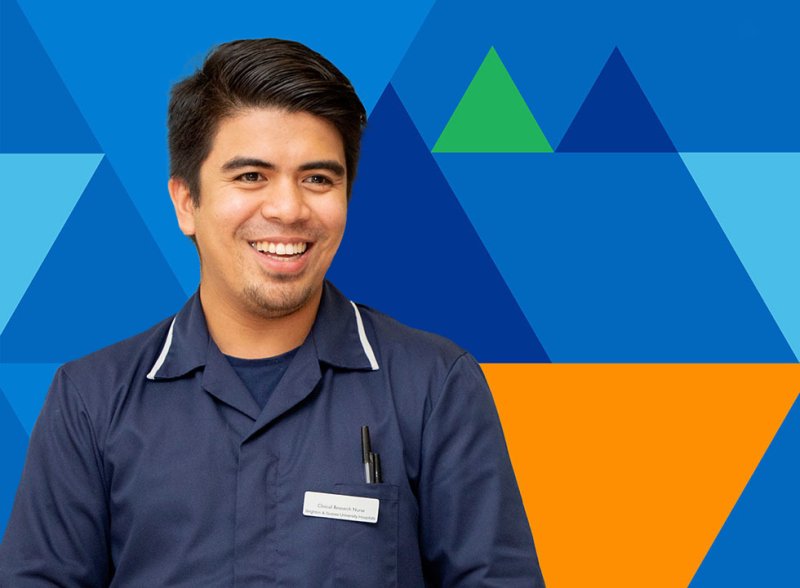 A man in dark blue NHS nursing uniform against UHSussex's bold triangle pattern background in shade of NHS blue and triangles in accents of orange and green. 